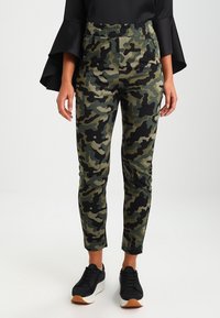 Kamouflagebyxor i nyanser av grönt och svart, med en stretchig midja och en smal passform, i kombination med svarta sneakers.