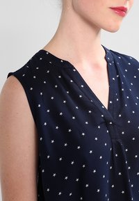 Marinblus med silverstjärnmönster, korta ärmar, V-ringning och slät yta, med en avslappnad passform och subtila sömnadsdetaljer.