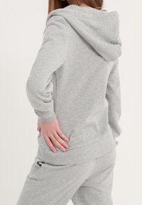 Sudadera gris con capucha, hecha de material suave. Cuenta con un corte relajado, puños acanalados y un bolsillo tipo canguro en el frente.