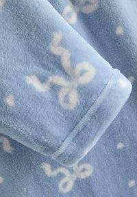 Niebieski polarowy materiał z wijącym się białym wzorem o miękkiej teksturze, wykończony mankietem z podwójnym szwem, nadający przytulny, ciepły wygląd.