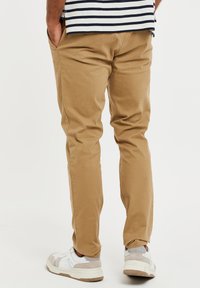 Vaaleat chinot, joissa on slim fit -leikkaus, sivutaskut ja sileä pinta. Yhdistettynä valkoisiin tennareihin, joissa on harmaita yksityiskohtia.