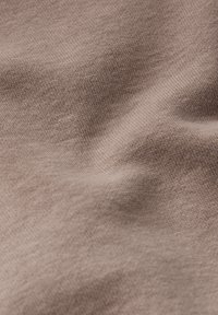 Tessuto morbido e leggero di un colore taupe tenue con una trama liscia, leggermente stropicciato che mostra il pattern di allungamento e tessitura.
