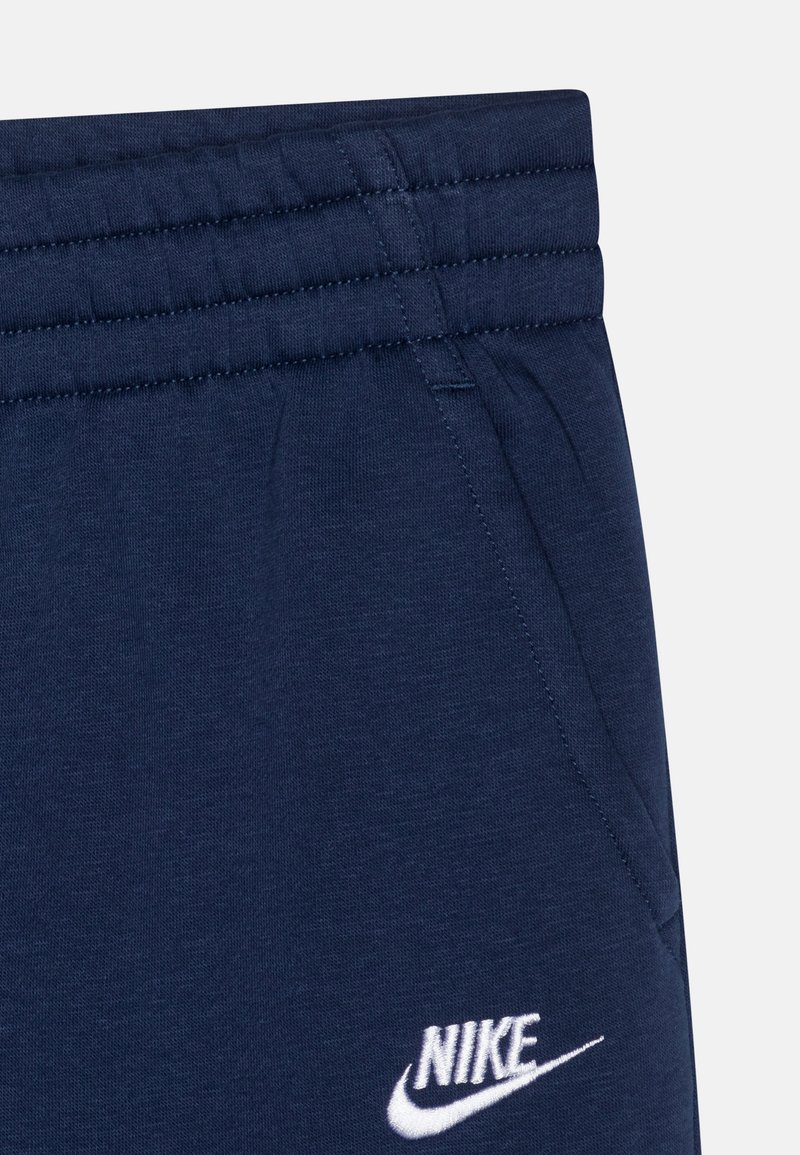 Dunkelblaue Baumwoll-Jogginghosen mit geripptem Bund, Seitentasche und weißem Nike-Logo, das auf der unteren linken Vorderseite gestickt ist.