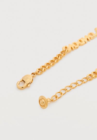 Βραχιόλι αλυσίδας από χρυσό με κούμπωμα και κυκλικό μενταγιόν, με λεία επιφάνεια και συνδεδεμένους κρίκους, που απεικονίζει τη λέξη «vogue» με καλλιγραφικά γράμματα.
