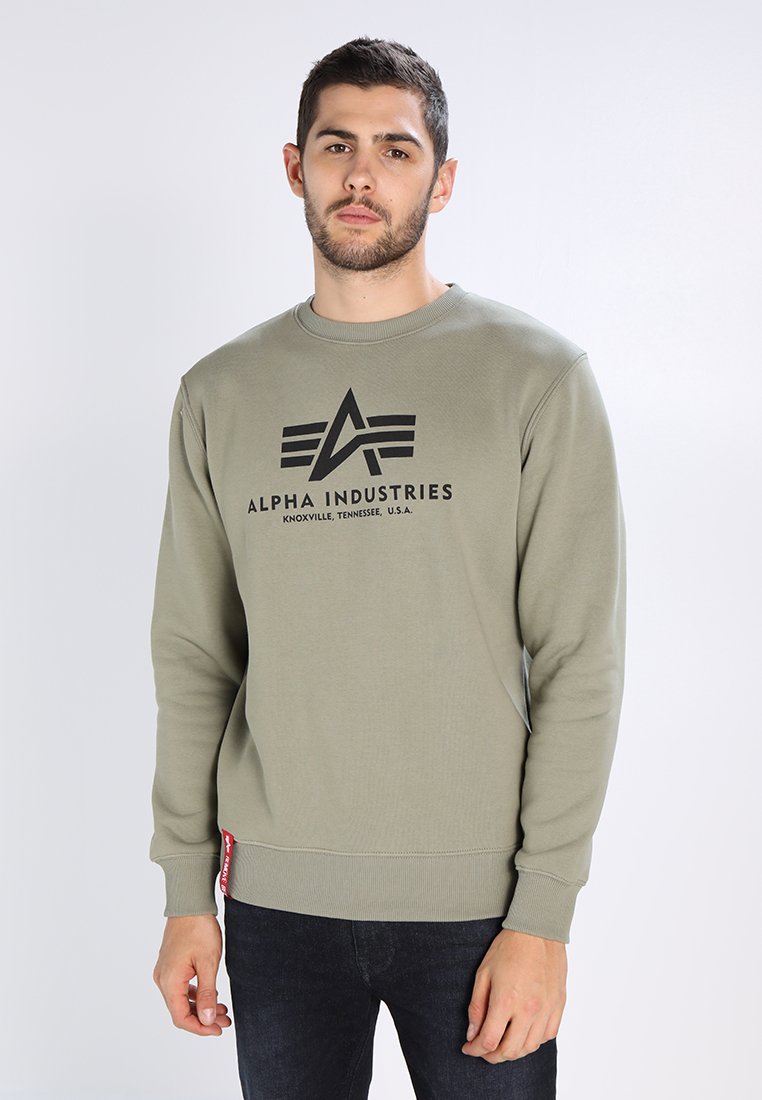 Sudadera color verde oliva hecha de algodón con puños y dobladillo de canalé. Presenta una impresión de logotipo negro en la parte delantera y una pequeña etiqueta roja en el costado.