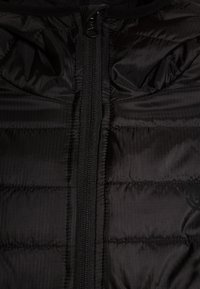 Czarna kurtka puchowa z poziomymi przeszyciami, wysokim kołnierzem i centralnym zamkiem błyskawicznym. Materiał ma delikatną fakturę i połysk.