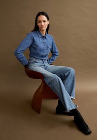 Hellblaue Jeanshemd mit Knopfleiste und einer Brusttasche, kombiniert mit klassischen blauen weit geschnittenen Jeans und schwarzen Stiefeletten.