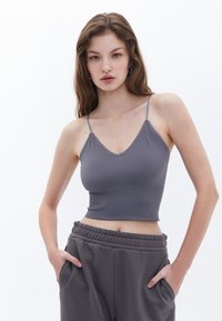 Top corto gris de canalé con tirantes finos y diseño de escote en V. Combinado con pantalones de chándal grises sueltos que cuentan con una cinturilla elástica y bolsillos.