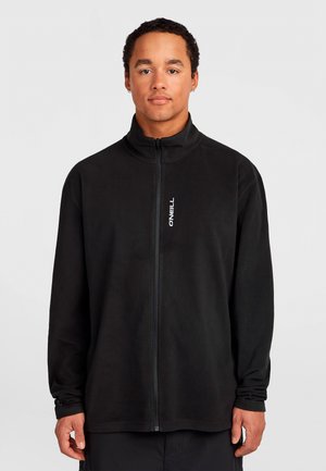 Young man with short curly hair wearing a black zip-up jacket with a high collar and small white O’Neill logo on chest.