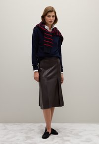 Marineblauwe trui met rode strepen, crèmekleurig overhemd met kraag eronder, bruine leren midirok en zwarte schoenen. Gladde texturen, op maat gemaakte pasvorm.