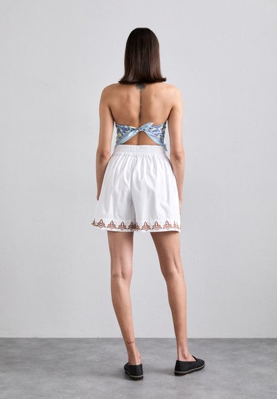 White shorts with elastic waistband, featuring a brown decorative trim. Blue floral print crop top with a twisted back design.