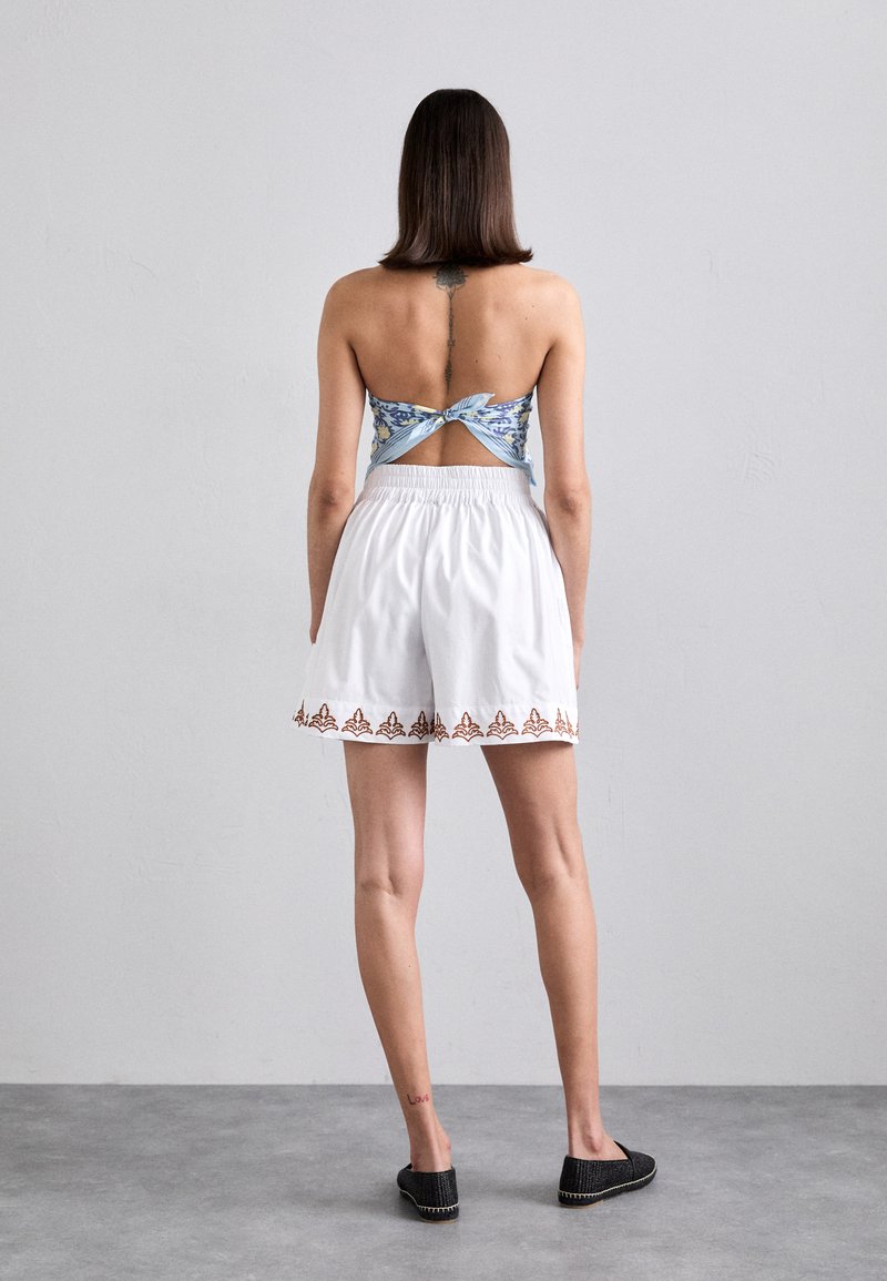 White shorts with elastic waistband, featuring a brown decorative trim. Blue floral print crop top with a twisted back design.