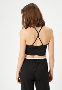Top corto negro con un diseño ajustado, tirantes de espalda nadador y detalles fruncidos en la parte posterior, combinado con pantalones negros sueltos que cuentan con una cinturilla elástica.