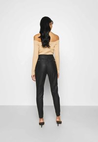 Zwarte leren broek met een hoge taille en taps toelopende benen, met een gladde textuur en twee achterzakken met rits. Gestyled met een naakt off-the-shoulder top.