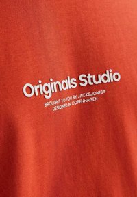 Rød bomulds T-shirt med hvid trykt tekst: "Originals Studio," "Bragt til dig af JACK&JONES," og "Designet i København."
