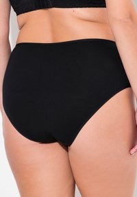 Mutande nere a vita alta realizzate in un tessuto morbido e elastico, con bordi lisci e senza cuciture visibili, progettate per comfort e copertura.