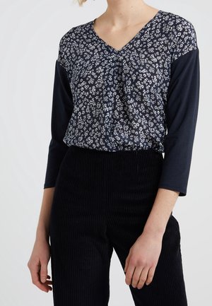 Top blu navy con motivo floreale, scollatura a V e maniche a tre quarti, abbinato a pantaloni in corduroy neri con texture.