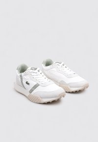 Zapatillas deportivas blancas con superficies texturizadas, acentos en gris claro, suela de goma con un patrón dentado, diseño con cordones y un pequeño logo verde en el lateral.