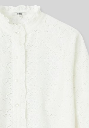 Blouse blanche en tissu texturé avec broderie florale, col à volants et fermetures à boutons sur le devant.
