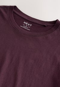 Burgundia värvi puuvillane kitsas lõikega T-särk, mis on varustatud ümmarguse kaelusega, pehme tekstuuri ja kaeluse juures oleva sildiga.