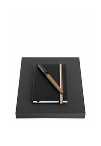 Carnet noir avec élastique à rayures blanches et marron, surmonté d'un stylo noir et marron, posé sur une surface carrée noire.