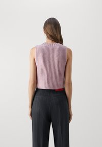 Haut en tricot sans manches, en rose clair, avec une texture côtelée et un col rond. Associé à un pantalon à rayures foncées. Vue de dos affichée.