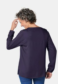Maglietta a maniche lunghe blu navy con scollatura rotonda, spacchi laterali e texture morbida; orlo leggermente più lungo sul retro rispetto al fronte.