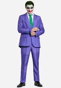 Completo a righe viola con dettagli verdi, camicia bianca e cravatta verde. Viso truccato con trucco bianco, rosso e verde scuro. Scarpe nere.