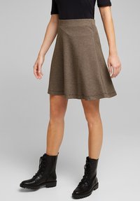 Bruine geruite flairrok van textuurstof, met een middelhoge tailleband en een gladde zoom, gecombineerd met zwarte veterschoenen met een militaire uitstraling.