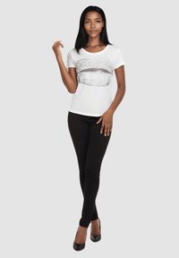 Camiseta blanca de manga corta con un diseño de labios plateados con lentejuelas en el frente, combinada con jeans pitillo negros y tacones altos negros.