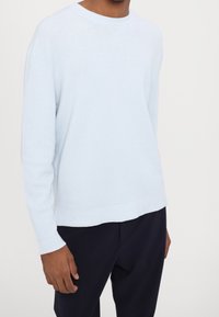 Jasnoniebieski sweter dziany o prążkowanej fakturze, z okrągłym dekoltem i lekko luźnym krojem. Zestawiony z ciemnymi spodniami dla kontrastu.