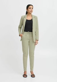 Hele rohelise kohandatud pintsak, millele on lisatud sobivad dressipüksid, elastne vöökoht ja stringiga, ning must fitted topp. Lihtne disain.