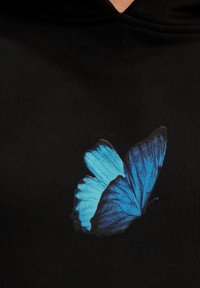 Sudadera de tela negra con un gran gráfico de una mariposa azul en la parte frontal, mostrando tonos vívidos y patrones intrincados en las alas.