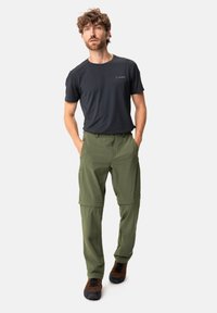 Pantaloni da escursionismo verde oliva con zip, realizzati in un tessuto leggero e a asciugatura rapida; abbinati a una maglietta a maniche corte grigio scuro e calzature marroni.