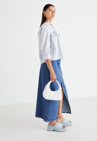 Sac à main matelassé blanc, jupe maxi en denim bleu avec une fente à l'avant, et sandales à plateforme bleu clair. Blouse à manches bouffantes rayée avec un col haut.