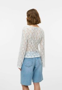 Valge pitsiline pikkade varrukatega topp, millel on lillemuster ja ümmargune kaelus, koos helesiniste denim lühikeste pükstega, millel on klassikaline lõige ja taskud.