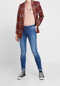 Červený kostkovaný blazer, světle růžové tričko s grafikou Eiffelovy věže, roztrhané modré skinny džíny a černé vysoké tenisky.