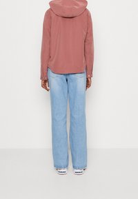 Rosa Kapuzenjacke mit lockerem Schnitt, kombiniert mit hellblauen, weit geschnittenen Jeans. Die Jacke ist mit Druckknöpfen versehen und hat eine weiche Textur.