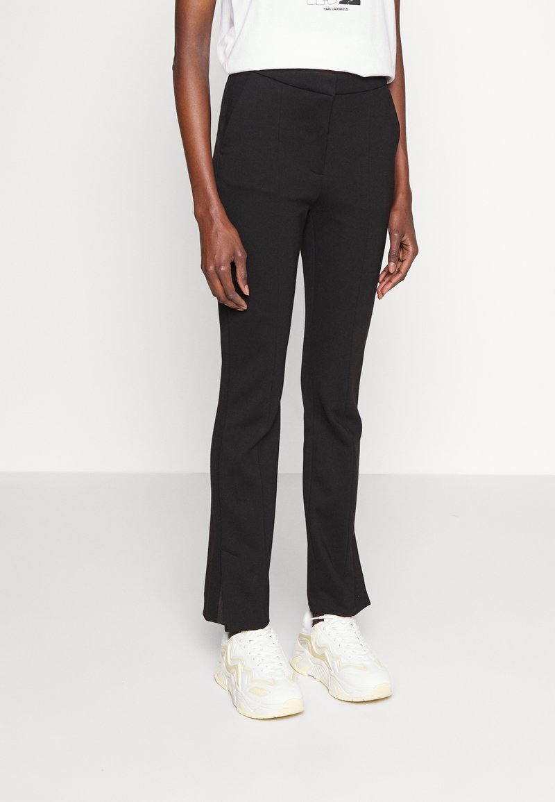 Black tailored trousers with a straight fit, featuring a smooth texture and subtle seam details, paired with white sneakers.