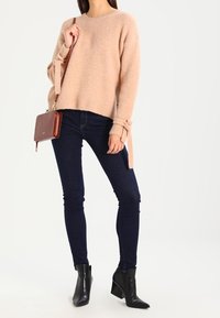 Ljusrosa tröja med sidoknytningar, rund halsringning, tillsammans med mörkblå skinny jeans och svarta ankelboots. Brun axelremsväska med klaff.