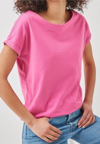 Camiseta rosa de manga corta de algodón con cuello redondo y puños enrollados, combinada con jeans de mezclilla azules.