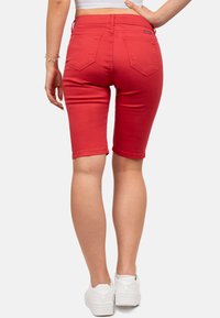 Rode denim Bermuda shorts met een strakke pasvorm, omgeslagen zoom en twee achterzakken, gecombineerd met witte sneakers.