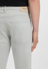 Jasnoszare bawełniane spodnie o gładkiej teksturze, z widocznym przeszyciem, dwoma tylnymi kieszeniami oraz beżową skórzaną metką z logo "BOSS".