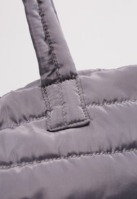 Close-up of a stitched gray padded fabric bag handle attached to the bag body with reinforced sewing.