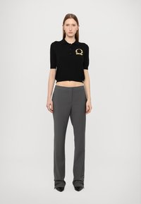 Polo negru scurt cu mâneci scurte, având un logo auriu. Asortat cu pantaloni gri, structurați, cu accente cu nasturi la baza.