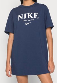 Navy modrá bavlněná tričko s uvolněným střihem, na přední straně s bílým textem a logem "NIKE". Krátké rukávy a kulatý výstřih.
