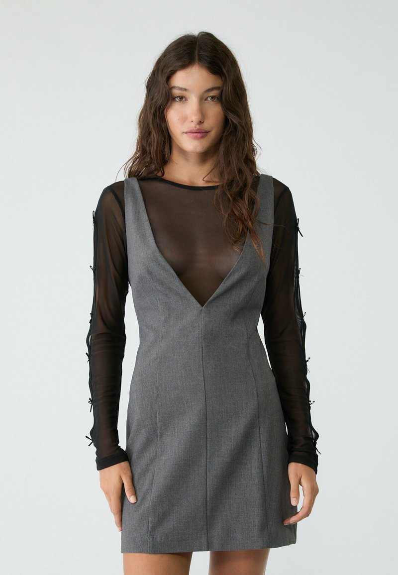 Abito grigio con scollo profondo, caratterizzato da maniche lunghe in organza nera trasparente con dettagli laterali. Tessuto liscio con una silhouette aderente.