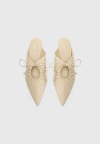 Mules de punta beige en cuero suave, con diseño recogido, corte ovalado y acentos atados en los lados.