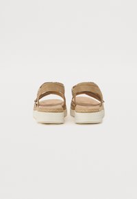 Sandales en suède marron avec des détails tissés, semelles blanches plates et ouverture à l'arrière. Le design présente un accent tressé le long des bords.