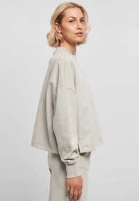 Lys grå overdimensjonert sweatshirt med lange ermer, sidesplitter og ribbede mansjetter. Myk tekstur og avslappet passform. Båret med matchende bukser.